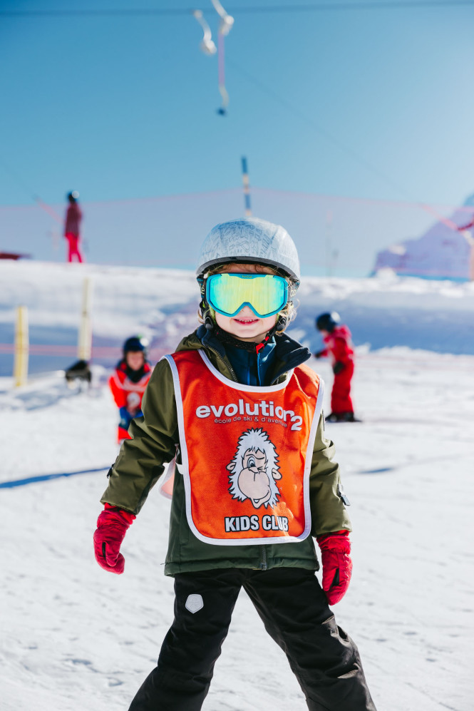 Child in the children’s ski area during a beginner ski lesson, wearing a helmet and goggles