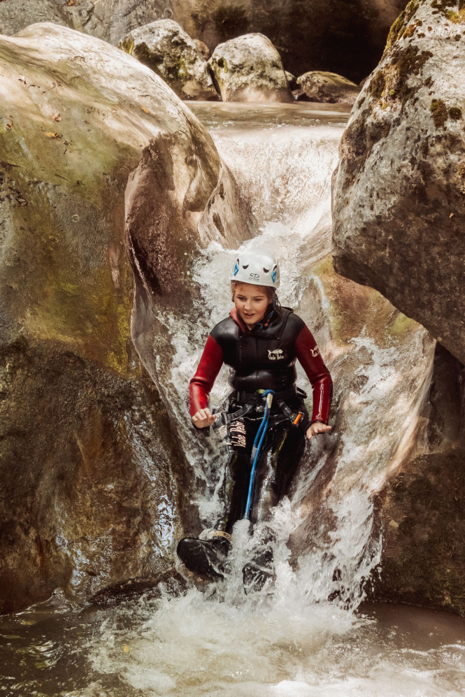 Child at a summer camp sliding down a natural rock slide during a canyoning activity in Megève
