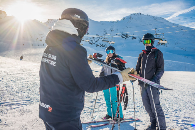 Moniteur de ski qui montre son ski à des élèves débutants adultes